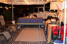 an outdoor table and chairs under a tent with lights on it in front of a white truck