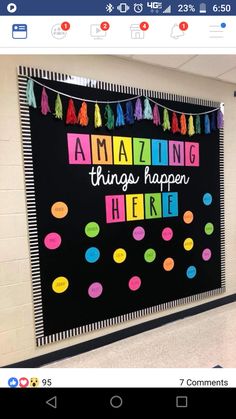 a bulletin board with the words amazing things happen here and colorful tassels on it