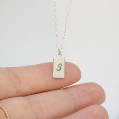 "A lovely display of your initials, or even a short word makes for a captivating look with our stylish tag pendant necklace. We will flawlessly engrave up to 2 letters on this sterling silver shiny pendant, beautifully complemented by an elegant and understated silver chain. NECKLACE DETAILS ⚬ Sterling silver rectangle tag and chain. ⚬ Rectangle measures 13.5mm x 6mm (.53\" x .23\"). ⚬ Chain in your choice of 16\", 18\", or 20\" length. ⚬ Spring ring clasp closure. ⚬ Personalized engraving of 1- Sterling Silver Hallmarked Initial Necklace For Anniversary, Classic Engraved Sterling Silver Charm Necklaces, Sterling Silver Stamped Necklace With Rectangular Pendant, Classic Sterling Silver Engraved Charm Necklace, Everyday Sterling Silver Engraved Charm Necklace, Classic Engraved Sterling Silver Charm Necklace, Classic Sterling Silver Charm Necklaces With Initials, Everyday Sterling Silver Initials Charm Necklace, Dainty Hallmarked Sterling Silver Charm Necklaces