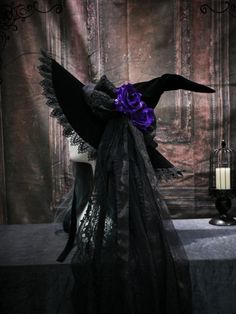 a table topped with a black and purple cloth covered headpiece next to a candle