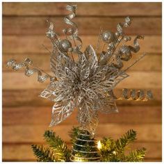 a christmas tree with silver decorations and lights on it in front of a wooden wall