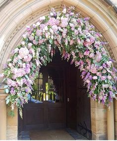 an archway with flowers hanging from it's sides in front of a stone building