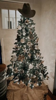 a christmas tree is decorated with silver and gold ornaments, while a cowboy hat sits on top