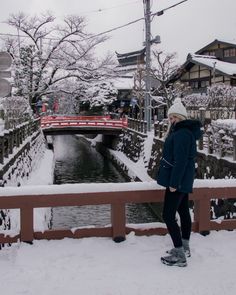 a woman standing on a bridge over a river in the snow with her back to the camera