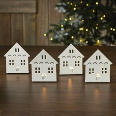 four small white houses sitting on top of a wooden table next to a christmas tree