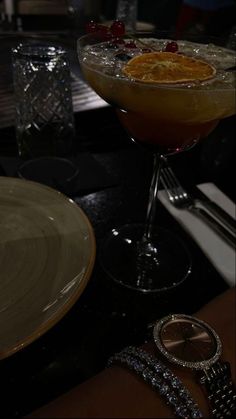 an orange drink with garnishes in a glass on a table next to a watch