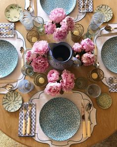 the table is set with plates, silverware and pink flowers