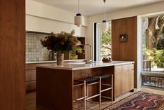 a kitchen with an island, sink and large window overlooking the trees in the back yard