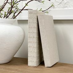 two white vases sitting next to each other on a wooden floor near a plant