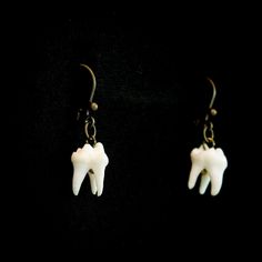 two tooth shaped earrings hanging from hooks on a black background, one is white and the other is brown