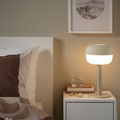 a lamp on a nightstand next to a bed with two pictures above it and a glass in the foreground