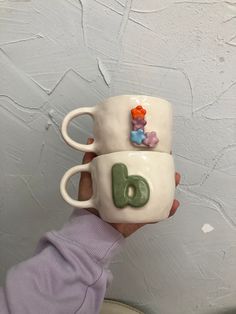 someone holding two coffee mugs in their hands with the letters d and e painted on them