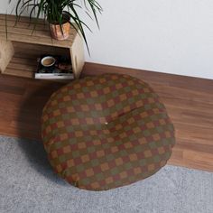 a brown and green checkered floor pillow sitting on top of a wooden table next to a potted plant