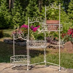 three tiered metal plant stands with pots on each shelf and flowers in the background