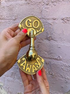 two hands are holding a brass bell with the word go san francisco on it, against a brick wall