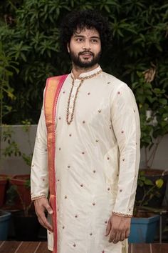 White pattu straight kurta with mandarin collar, full sleeves and floral butti pattern zardozi hand embroidery. Paired with cowl draped dhoti pant with pink kadhua border and a dupatta.
Component: 3
Pattern: Embroidered
Type Of Work: Zardozi and Kadhua Work
Neckline: Mandarin Collar
Sleeve Type: Full Sleeves
Fabric: Pattu
Color: White
Other Details: 
Pink borders
Side slits on kurta
Closure:
Kurta: Front button placket
Dhoti: Elastic waistband
Occasion: Groom, Wedding - Aza Fashions Navratri Bandhgala With Dori Work And Straight Kurta Style, Navratri Bandhgala With Dori Work, Sherwani With Dori Work For Navratri Puja, Navratri Sherwani With Dori Work For Puja, Chanderi Sherwani With Cutdana For Traditional Ceremonies, White Chanderi Sherwani For Puja, Cutdana Chanderi Sherwani For Traditional Ceremonies, Sherwani With Cutdana For Traditional Ceremonies, Traditional Sherwani With Dori Work For Navratri