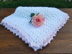 a crocheted blanket with a pink rose on it sitting on top of a wooden table