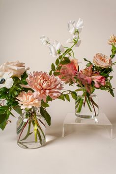 two clear vases filled with flowers on top of a white table next to each other