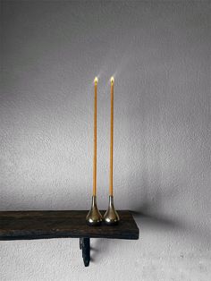 two candles sitting on top of a wooden shelf