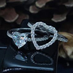 two heart shaped diamond rings sitting on top of a black box with shells in the background