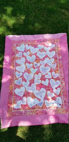 a pink quilt with hearts on it sitting in the grass