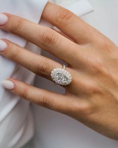 a woman's hand with a diamond ring on her finger and white shirt in the background