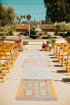 an outdoor wedding ceremony with wooden chairs and rugs on the aisle leading up to the altar