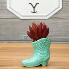 a green boot with a red flower in it sitting on a wooden table next to a sign