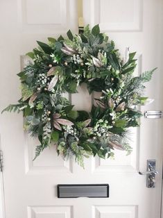 a white door with a wreath on it and some green leaves hanging from the front