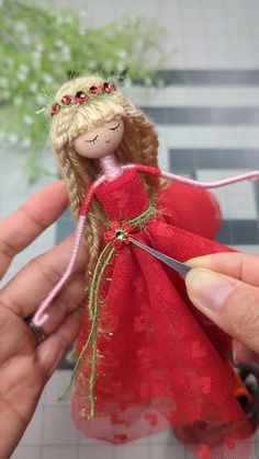 a hand holding a doll with a red dress and tiara