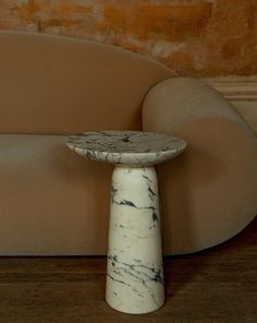 a white marble table sitting on top of a wooden floor next to a beige couch