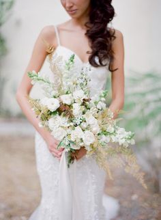 a woman in a white dress holding a bridal bouquet with greenery and flowers