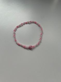 a pink beaded bracelet on a white surface with a red heart charm hanging from it's end