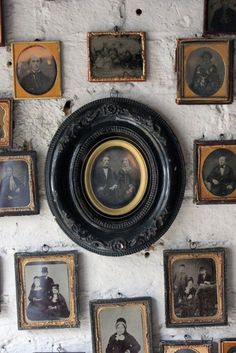 a wall with many framed pictures and an old fashioned plate hanging on it's side