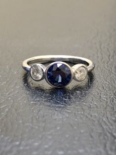 DeKara Designs Collection Beautiful Modern/Art Deco Ceylon Blue Sapphire and Diamond Ring Metal- 90% Platinum, 10% Iridium Stones- 1 Round Ceylon Blue Sapphire 1.00-1.05 Carats 6 MM, 2 Round Diamonds F-G VS2 Clarity, 0.40 Carats. Size-4-12 Classic and Timeless Art Deco Inspired Ceylon Blue Sapphire Diamond Three Stone Engagement Ring. There is a beautiful Ceylon Blue Sapphire that is extremely fiery and amazing in color that is featured as the center stone. The blue sapphire is professionally be Wedding Ring Sapphire, Blue Sapphire Engagement Ring, Ceylon Blue Sapphire, Sapphire Band, Three Stone Diamond, Sapphire Engagement Ring Blue, Engagement Rings Platinum, Blue Sapphire Diamond, Sapphire Engagement Ring