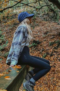 a woman leaning on a rail in the woods with leaves all over her and wearing boots