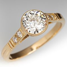 a diamond ring with three stones on the band and an oval shaped center stone in yellow gold