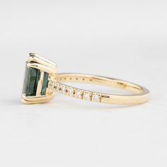 a gold ring with an emerald and diamond band on the side, in front of a white background