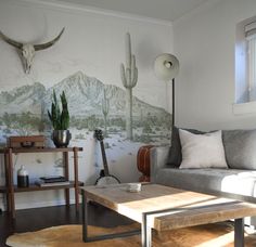 a living room with a couch, coffee table and cactus wall mural on the wall