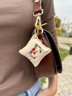 a woman wearing a brown shirt holding a small purse with a cross - stitched design on it