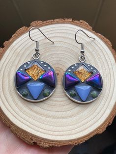 Hand crafted mosaic earrings.  Geometric style with gold foil, iridescent purple/black, and periwinkle glass tiles. Little Jade Gemstones and tiny silver bead accents.  Finished with charcoal gray grout.  Round dangle measures approximately 1 inch long (not including hooks). Earring hooks and setting are made out of hypoallergenic stainless steal. Gray Grout, Mosaic Earrings, Iridescent Purple, Stainless Steal, Glass Tiles, Earrings Geometric, Earrings Bohemian, Silver Bead, Earring Hooks