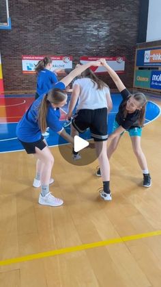 three girls in blue shirts and black shorts on a basketball court with one girl holding the ball