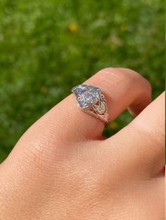 a woman's hand with a ring on it and green grass in the background