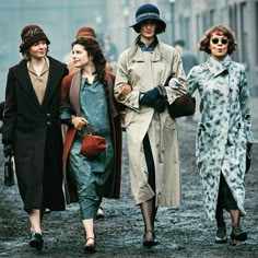 three women are walking down the street in coats and hats, one is carrying a purse