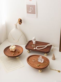 three wooden trays sitting on top of a white table next to a vase and necklace