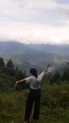 a man standing on top of a lush green hillside with his arms in the air