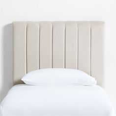 a bed with a white headboard and pillows on it's sides, in front of a wall