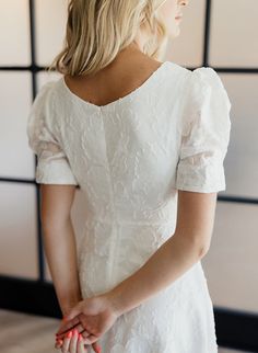 the back of a woman's head wearing a white dress and holding her hand on her hip