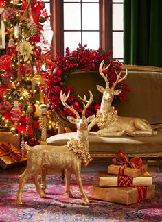 two golden deer figurines sitting in front of a christmas tree with presents under it