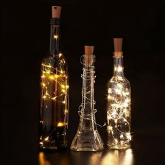 three wine bottles with lights in them on a black surface, one is empty and the other has a cork